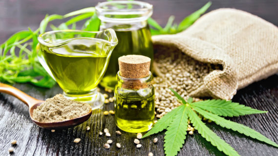 Hemp oil in two glass jars and sauceboat with grain in the bag, leaves and stalks of cannabis, a spoon with flour on the background of wooden boards (Hemp oil in two glass jars and sauceboat with grain in the bag, leaves and stalks of cannabis